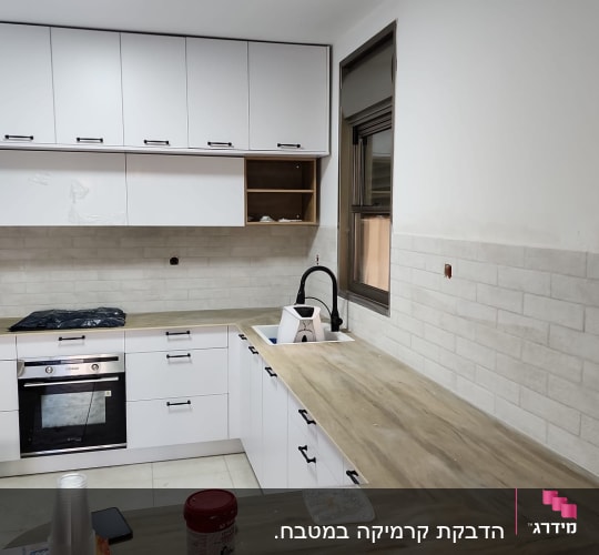 מטבח חדש עם ארונות לבנים ומשטח עבודה מעץ